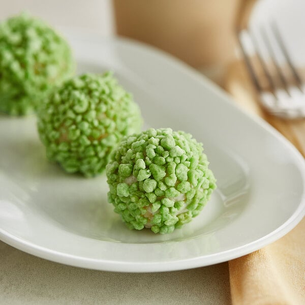 A white plate with a close-up of a green pistachio crumb ball on it.