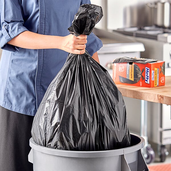 A woman holding a black Hefty garbage bag in a kitchen.