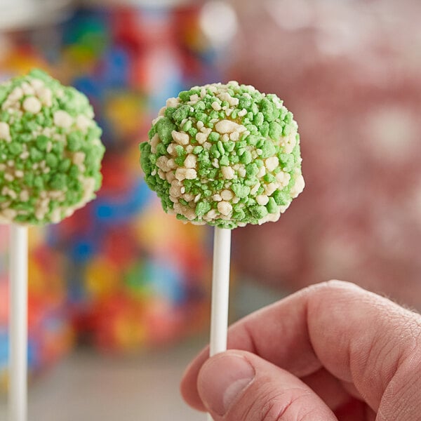 A hand holding green and white cake pops with Yum Crumbs Key Lime Pie crumb topping.