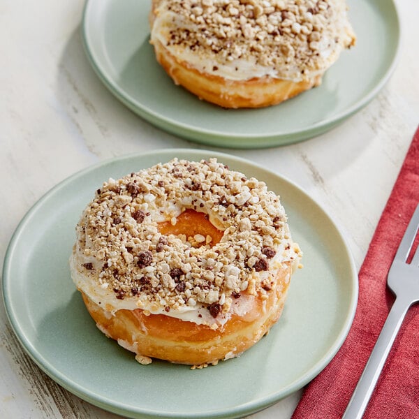 A plate with a donut topped with frosting and nuts next to a fork and knife on a red cloth.