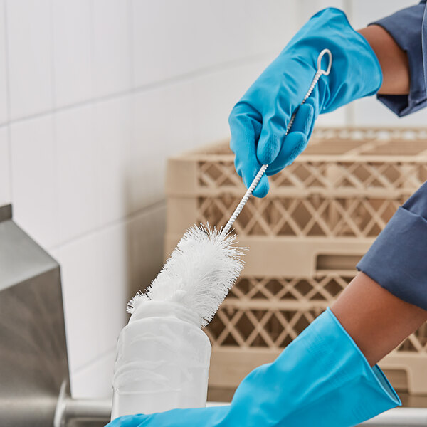 A person in blue gloves using a white O-Cedar glass and bottle brush to clean a sink.