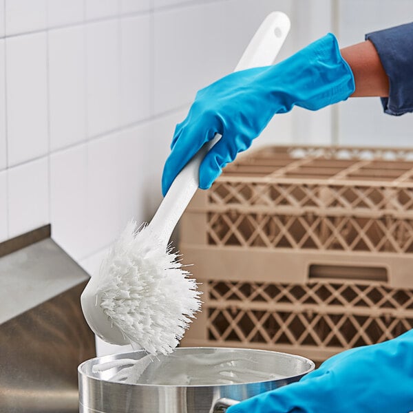 A person in blue gloves using a white O-Cedar utility brush to clean a silver pot.