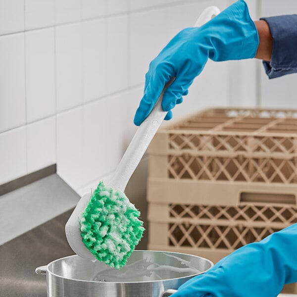 A person in blue gloves cleaning a pot with a green and white O-Cedar utility brush.