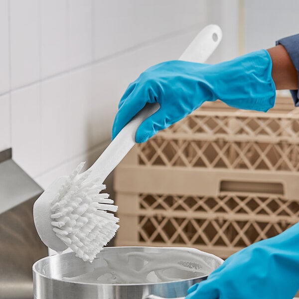 A person in blue gloves using a white O-Cedar utility brush to clean a pot.