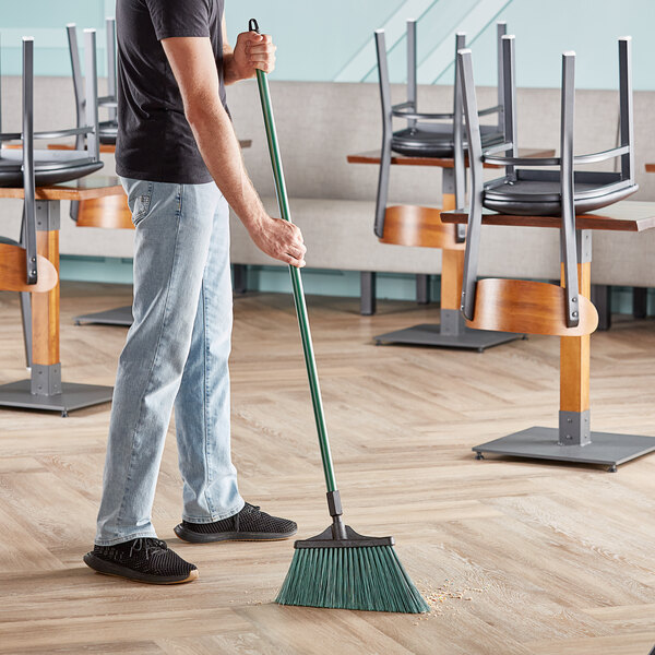 A man using an O-Cedar commercial angle broom with green bristles to sweep the floor.