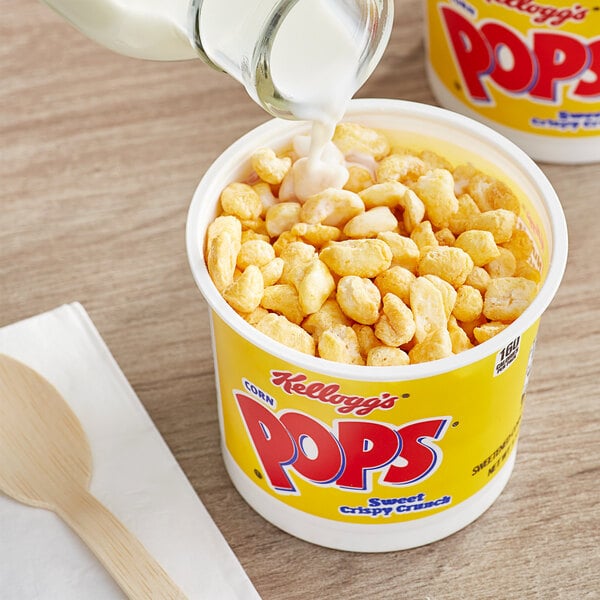 A container of Kellogg's Corn Pops cereal with a spoon pouring milk into it.