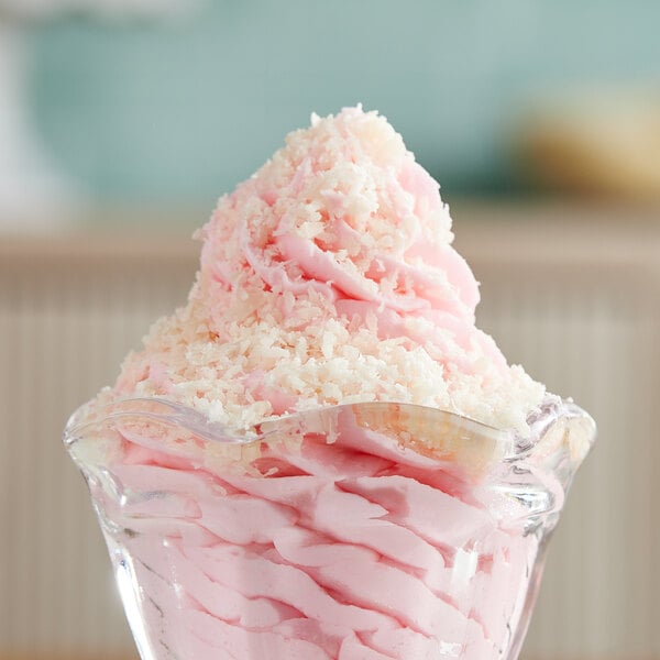 A glass bowl of pink ice cream topped with chipped coconut.