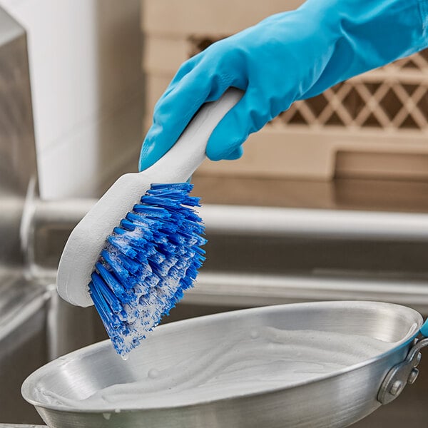 A person in blue gloves using an O-Cedar blue utility brush to clean a bowl of soap.