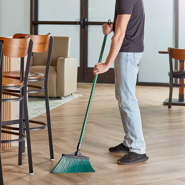 A person sweeping the floor with an O-Cedar Commercial green angle broom.