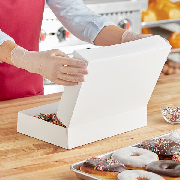 A woman opening a white Baker's Lane box of donuts on a counter.