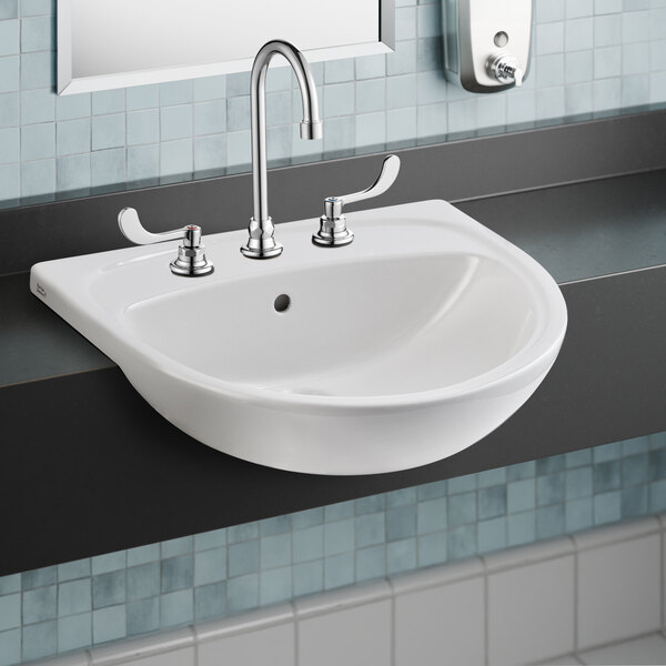 An American Standard white fireclay semi-countertop sink with silver faucets.