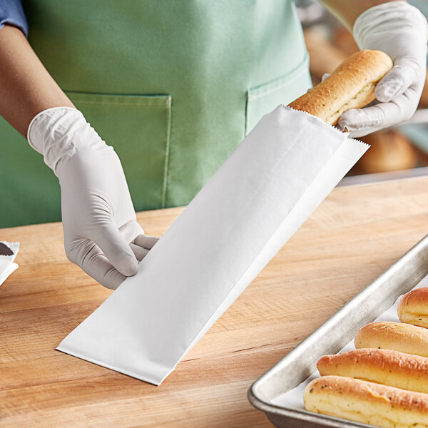 A person in white gloves holding a white insulated foil bread bag filled with a loaf of bread.