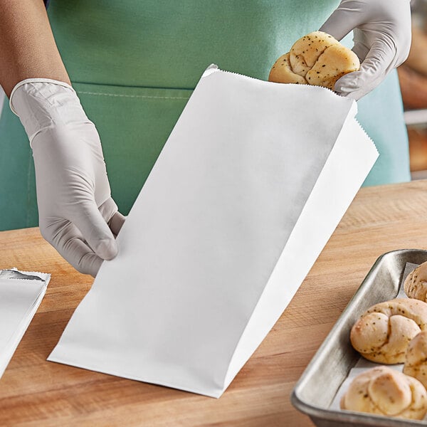 A person in gloves holding a white bag of bread.