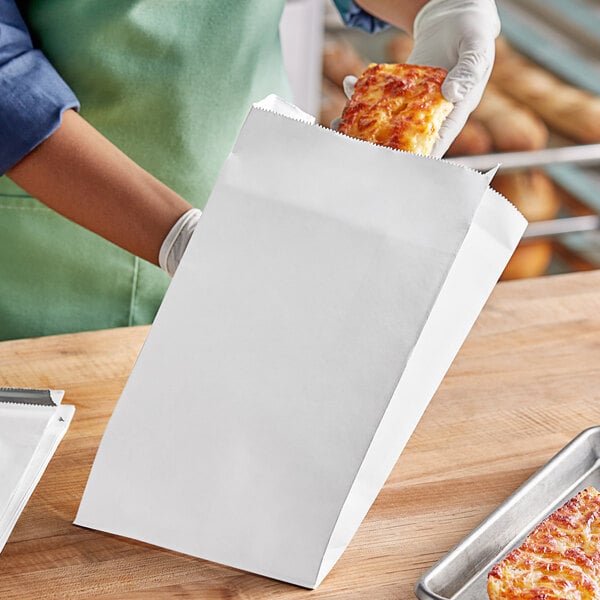 A person's hand holding a white Choice insulated foil bread bag containing food.