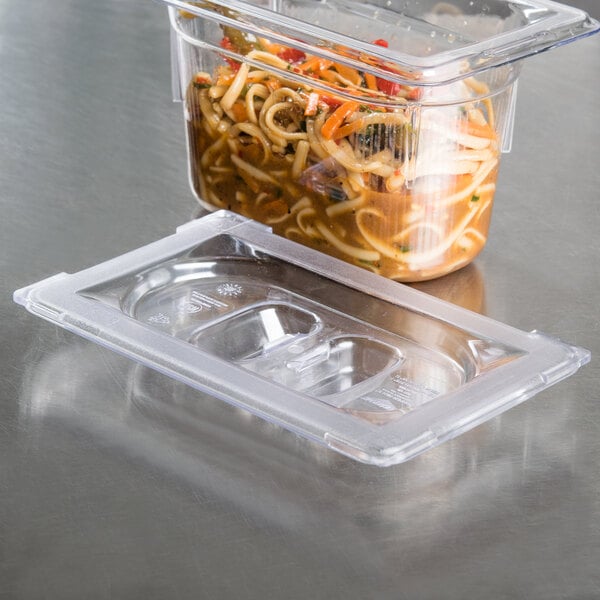 A Vollrath clear polycarbonate lid on a plastic food container filled with noodles and vegetables.