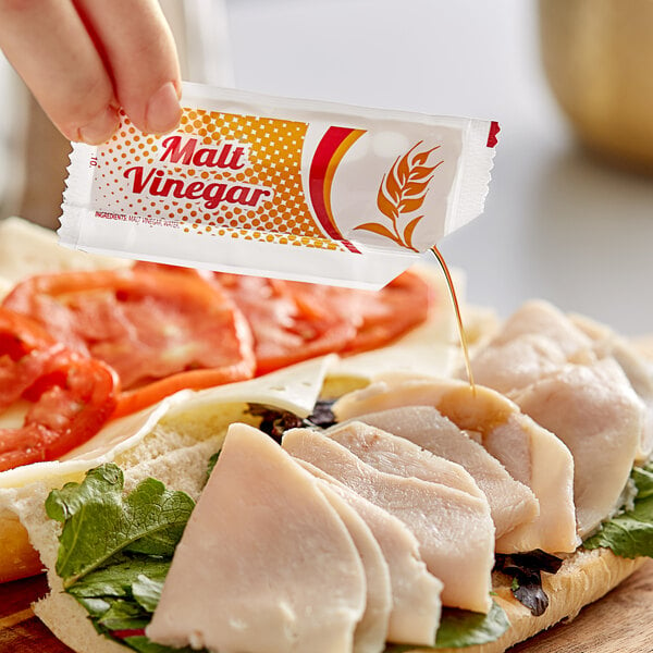 A person putting a Kari-Out Company Malt Vinegar packet on sliced chicken.