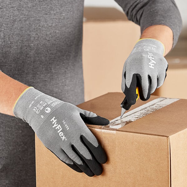 A person wearing Ansell HyFlex gloves using scissors to cut open a box.