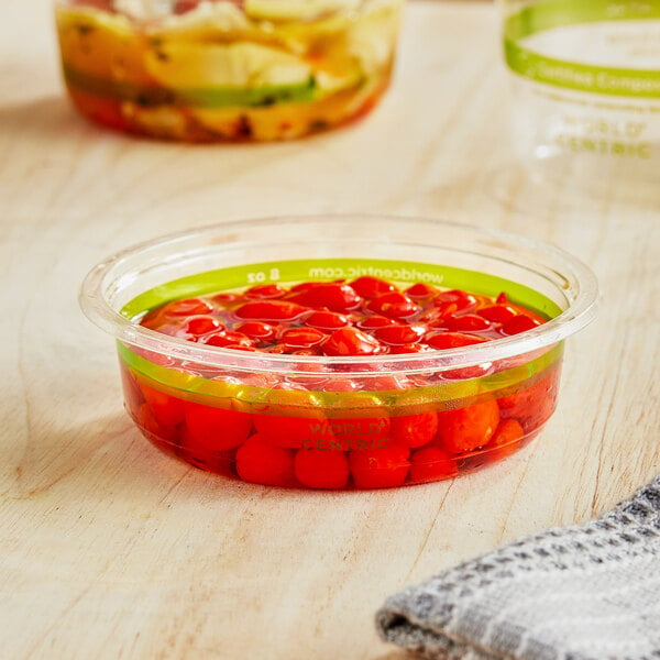 A World Centric compostable deli container filled with red tomatoes on a table.