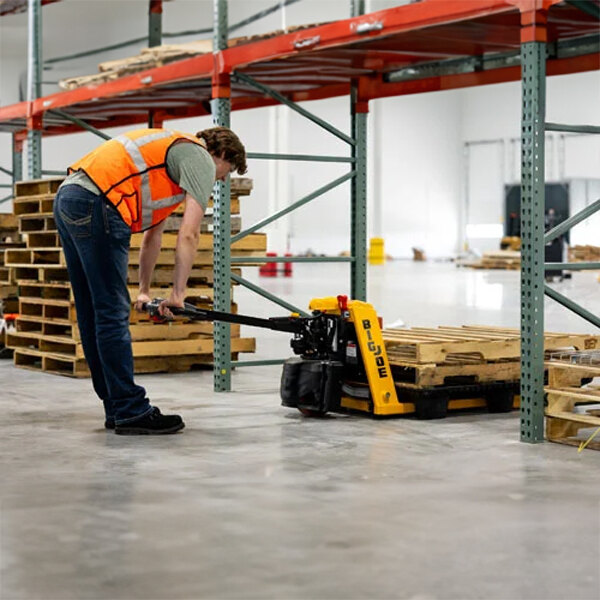 A man in a safety vest using a Big Joe semi-electric pallet jack in a warehouse.