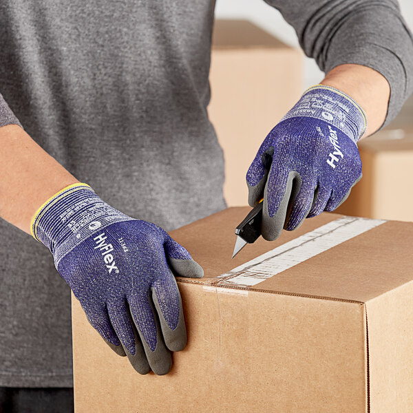 A person wearing blue Ansell HyFlex gloves cutting a box.