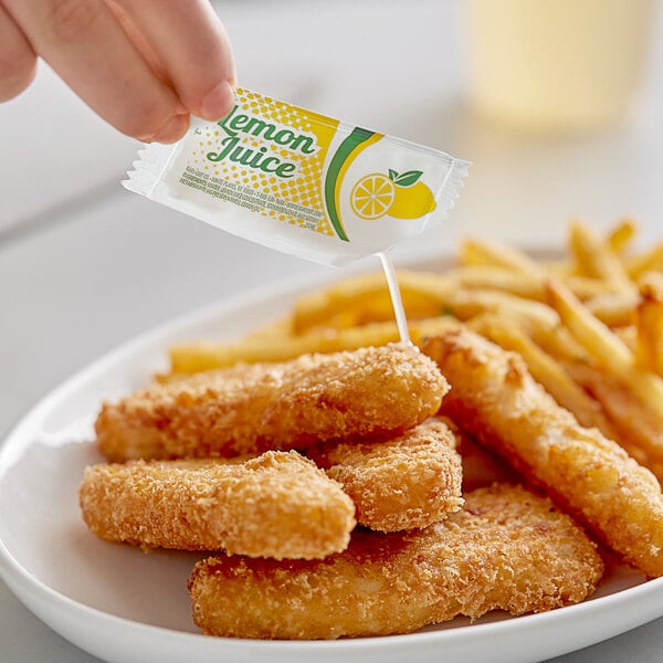 A hand holding a Kari-Out Company lemon juice packet over a plate of fried food.