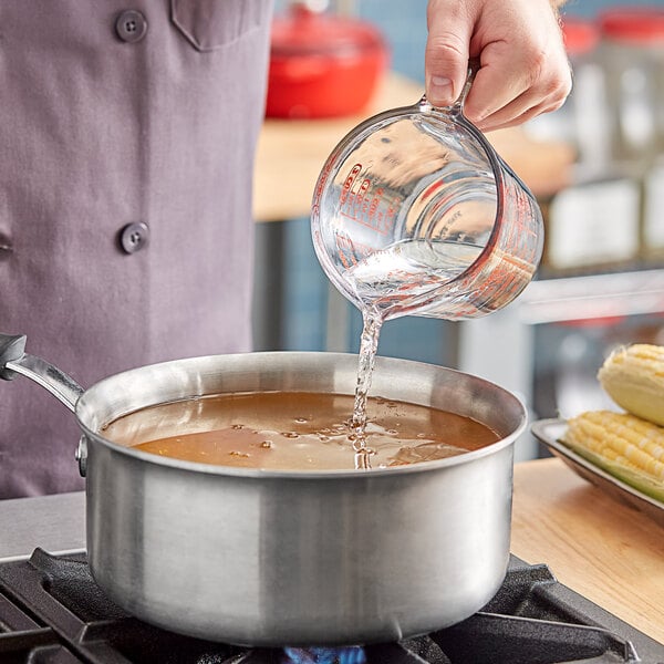 A person pouring Kari-Out Company Rice Cooking Wine into a pot of brown liquid.