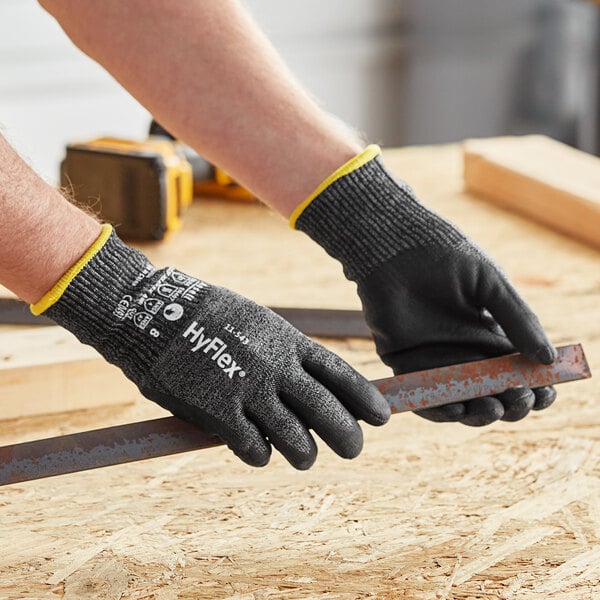 A person wearing Ansell HyFlex gloves holding a piece of metal.