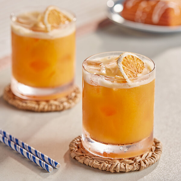 Two glasses of Les Vergers Boiron quince puree with straws on a table with pastries.