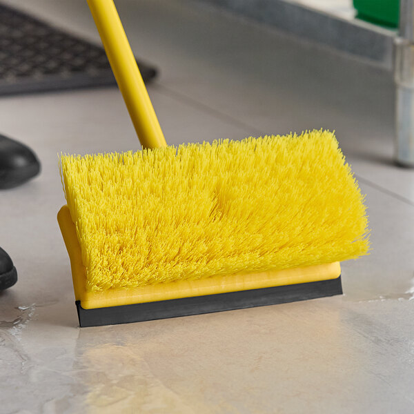 A Lavex yellow unflagged brush head with a squeegee being used on the floor.