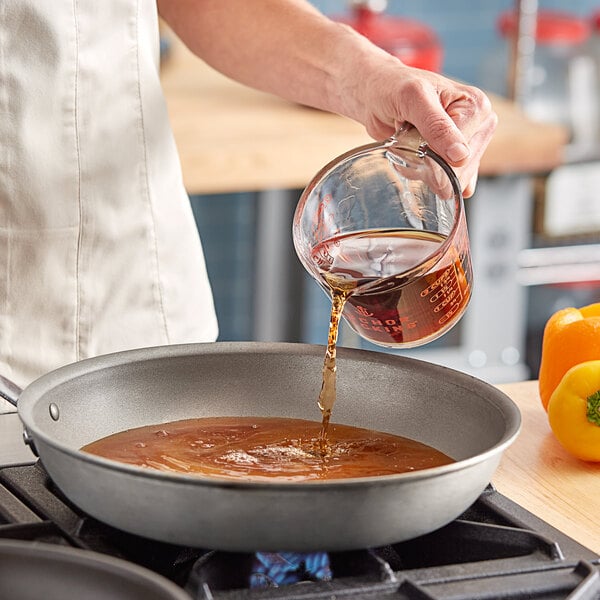 A person pouring brown cooking wine into a pan on a stove.