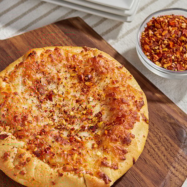A pizza on a cutting board next to a bowl of Kari-Out Company Crushed Red Chilies.