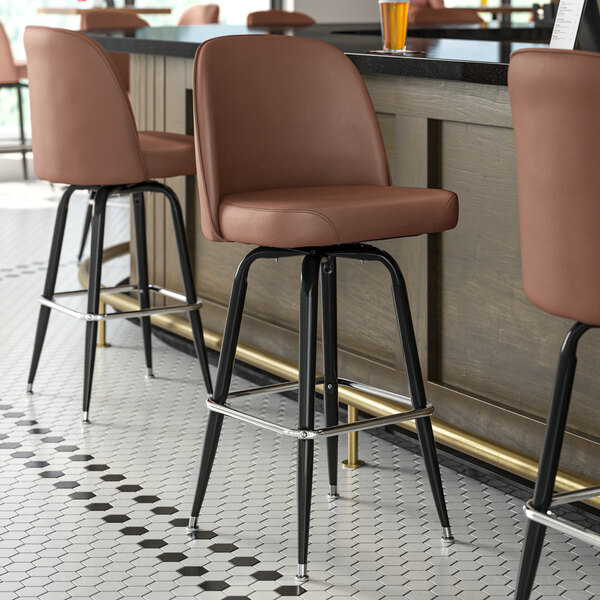 Lancaster Table & Seating black swivel barstools with dark brown vinyl bucket seats at a bar counter.