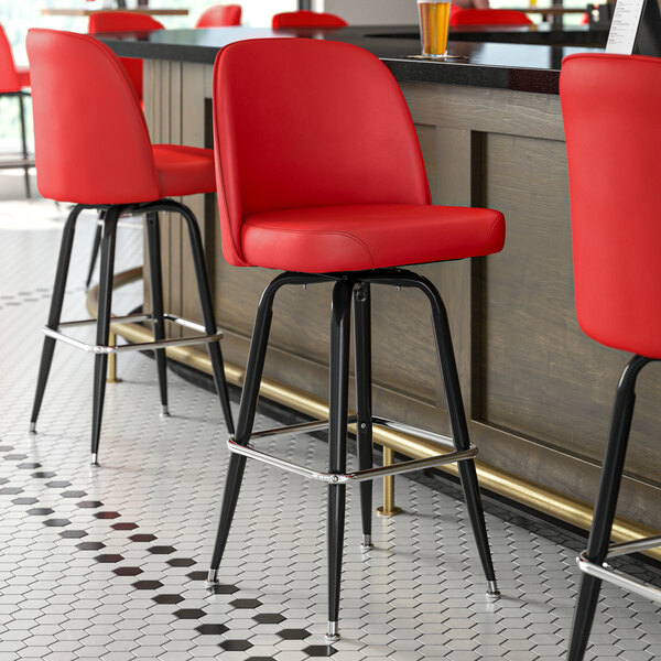 A row of red Lancaster Table & Seating bucket seat cushions on bar stools.