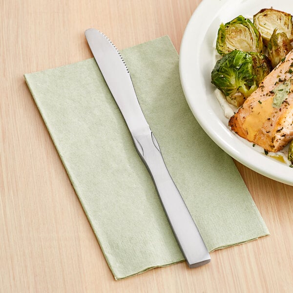 A Choice medium weight stainless steel dinner knife on a plate of food on a table.