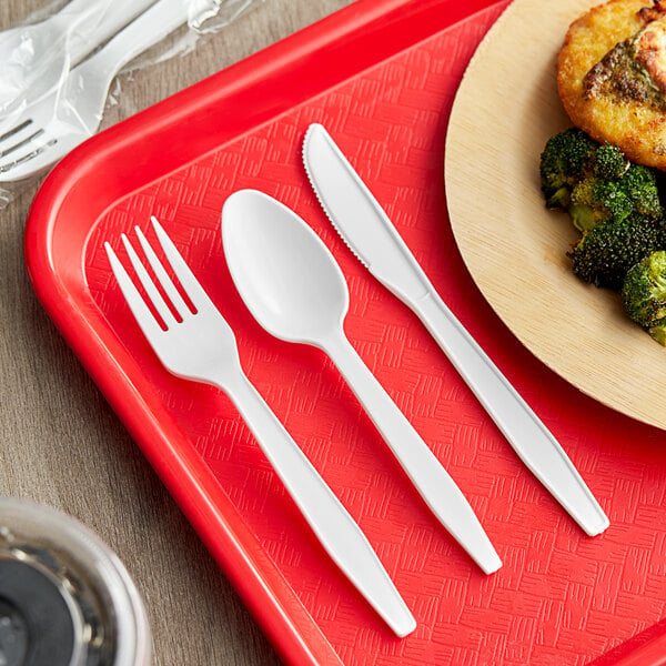 A red tray with a white plastic fork, knife, and spoon on a plate of food.