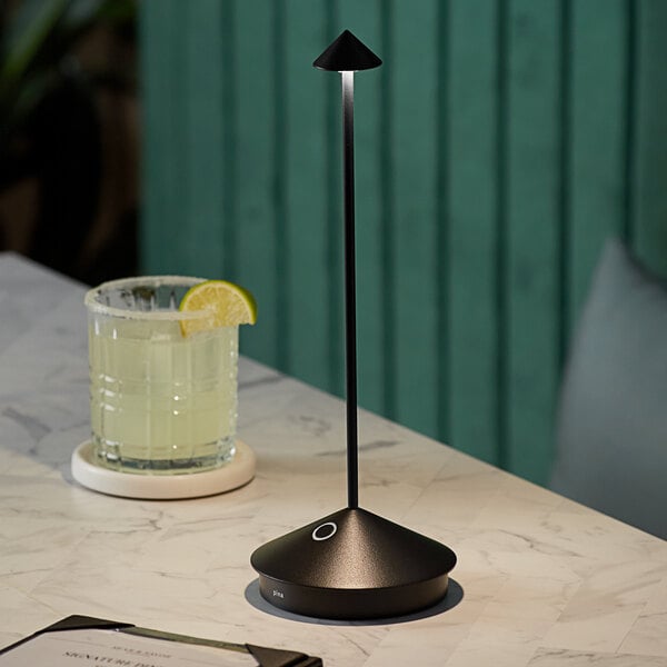 A Zafferano America black cordless table lamp on a table with a glass of lemonade and a lime.