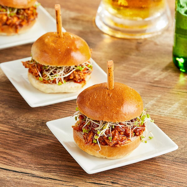 Three Bridor Brioche slider rolls with pulled pork on a white plate on a table.