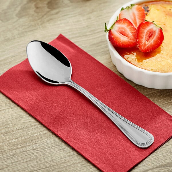 A Choice Milton stainless steel dinner spoon on a napkin next to a bowl of strawberries.