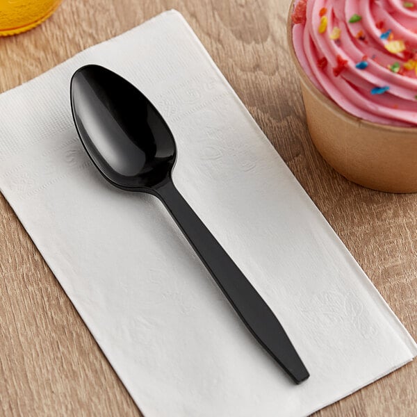 A black Choice plastic teaspoon on a white napkin next to a cupcake.