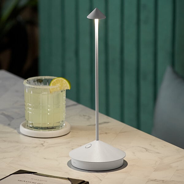 A Zafferano America white cordless table lamp on a table with a glass and a slice of lime.