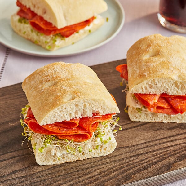 Sliced Bridor ciabatta baguette sandwiches with meat and sprouts on a cutting board.