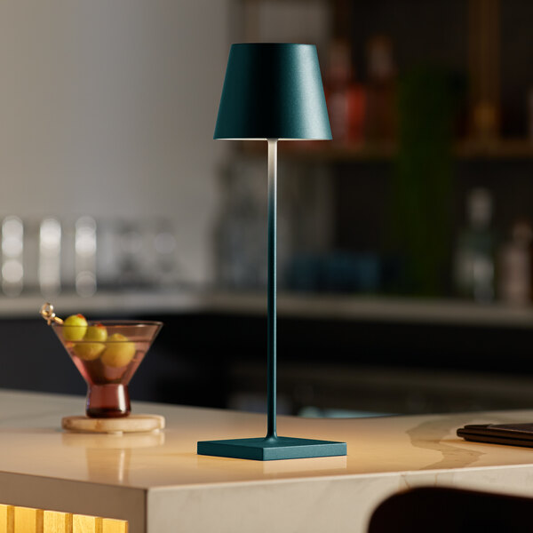 A Zafferano America Poldina Pro dark green cordless table lamp on a black and white table surface.