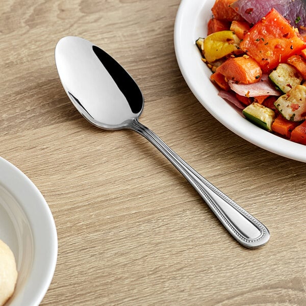 A white plate with a Choice Milton stainless steel serving spoon next to food.