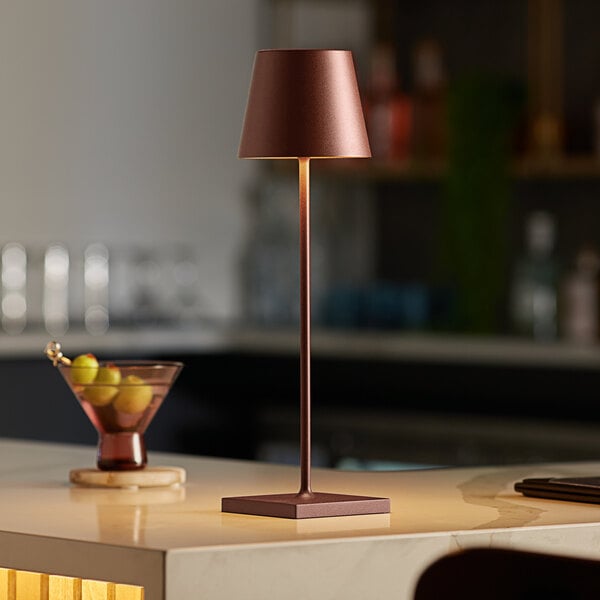 A Zafferano America Poldina Pro table lamp on a black counter top with a drink and fruit.