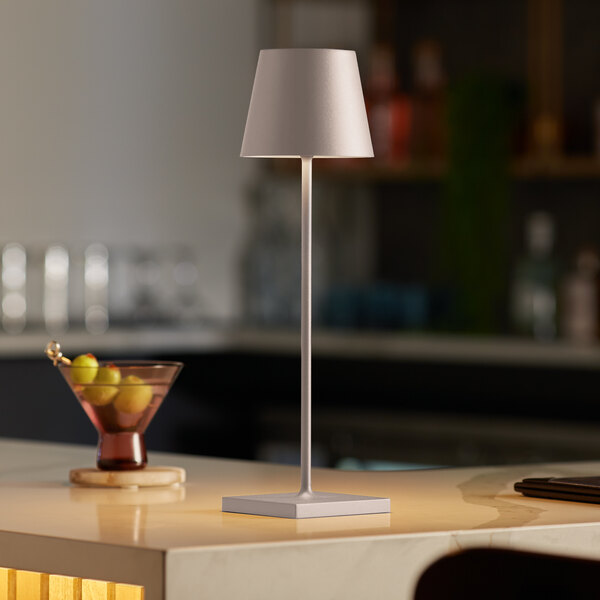 A Zafferano America Poldina Pro table lamp on a counter with a glass of wine and fruit.