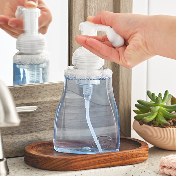 A person's hands using a Dial Spring Water foaming hand soap pump on a kitchen counter.