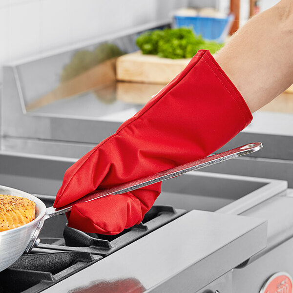 A person wearing a red Tucker Safety oven mitt removing food from an oven.