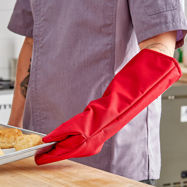 A person wearing a red Tucker Safety oven mitt holding a tray of food.