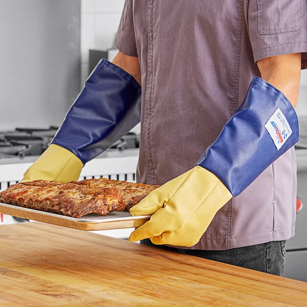 A man wearing yellow Tucker Safety oven gloves holding a tray of meat.