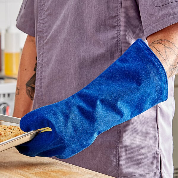 A person wearing a blue Tucker Safety oven mitt holding a tray of food.